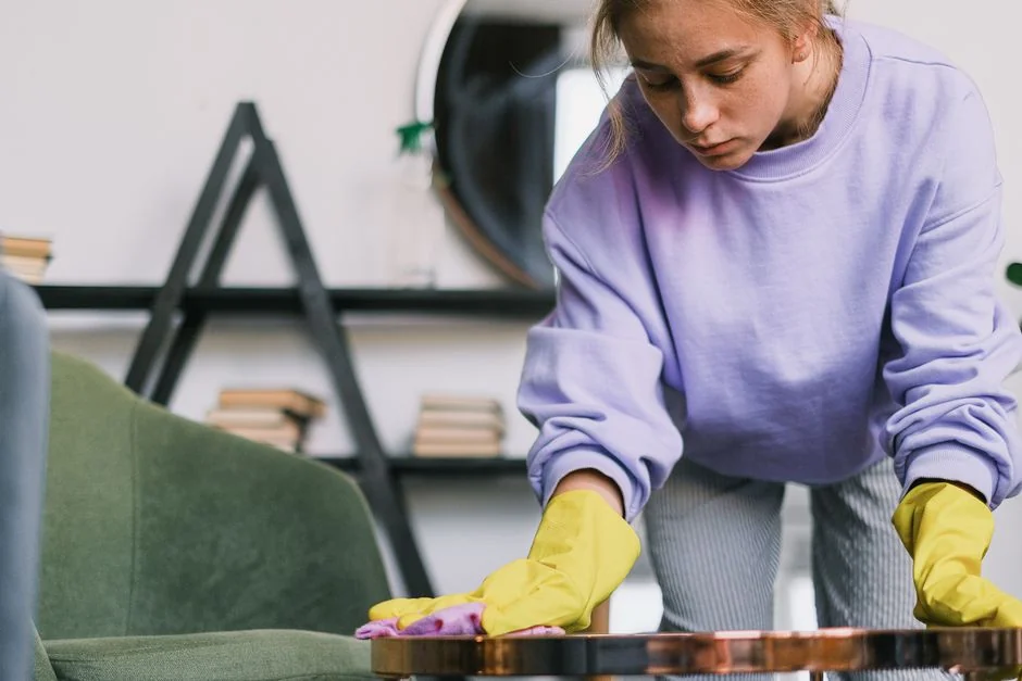a-woman-in-a-green-shirt-and-black-gloves-vacuuming-a-gray-ottoman-5txz228u4eo
